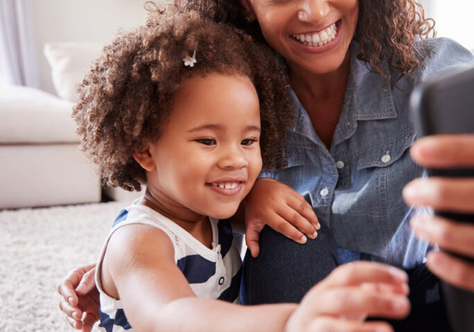 Mother,And,Toddler,Daughter,Looking,At,Photos,On,Smartphone