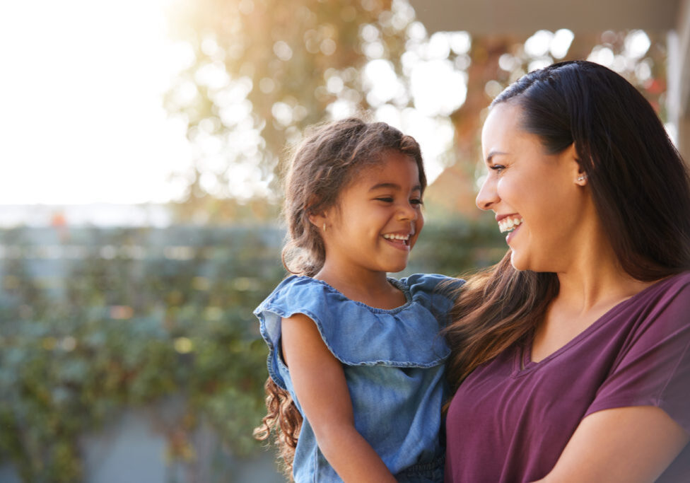 Smiling,Hispanic,Mother,Holding,Daughter,Laughing,In,Garden,At,Home